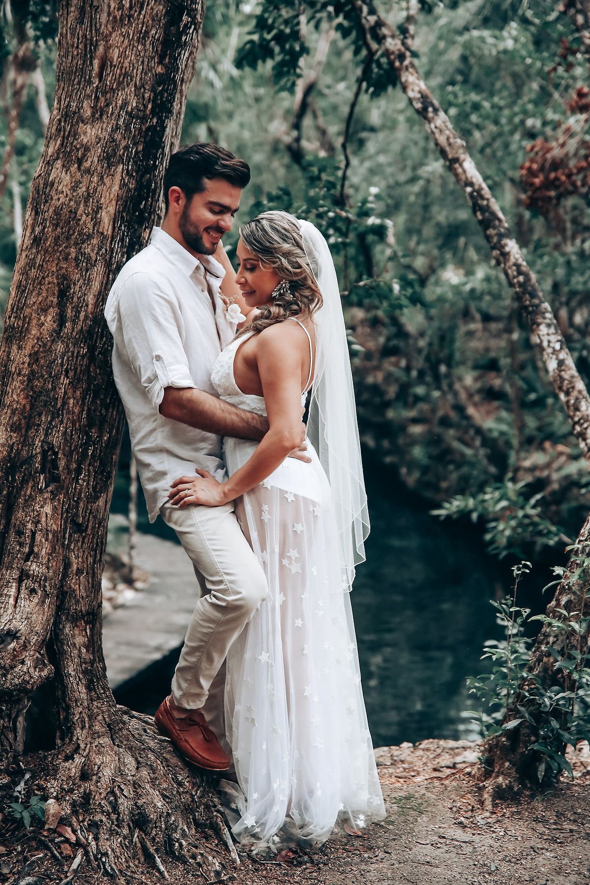 An intimate moment captured between newlyweds in white attire against a wooded backdrop.