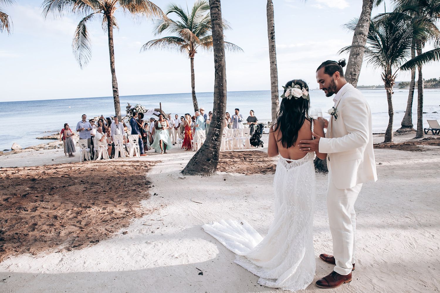 Beachside wedding celebration with palm trees and guests on a sunny day.