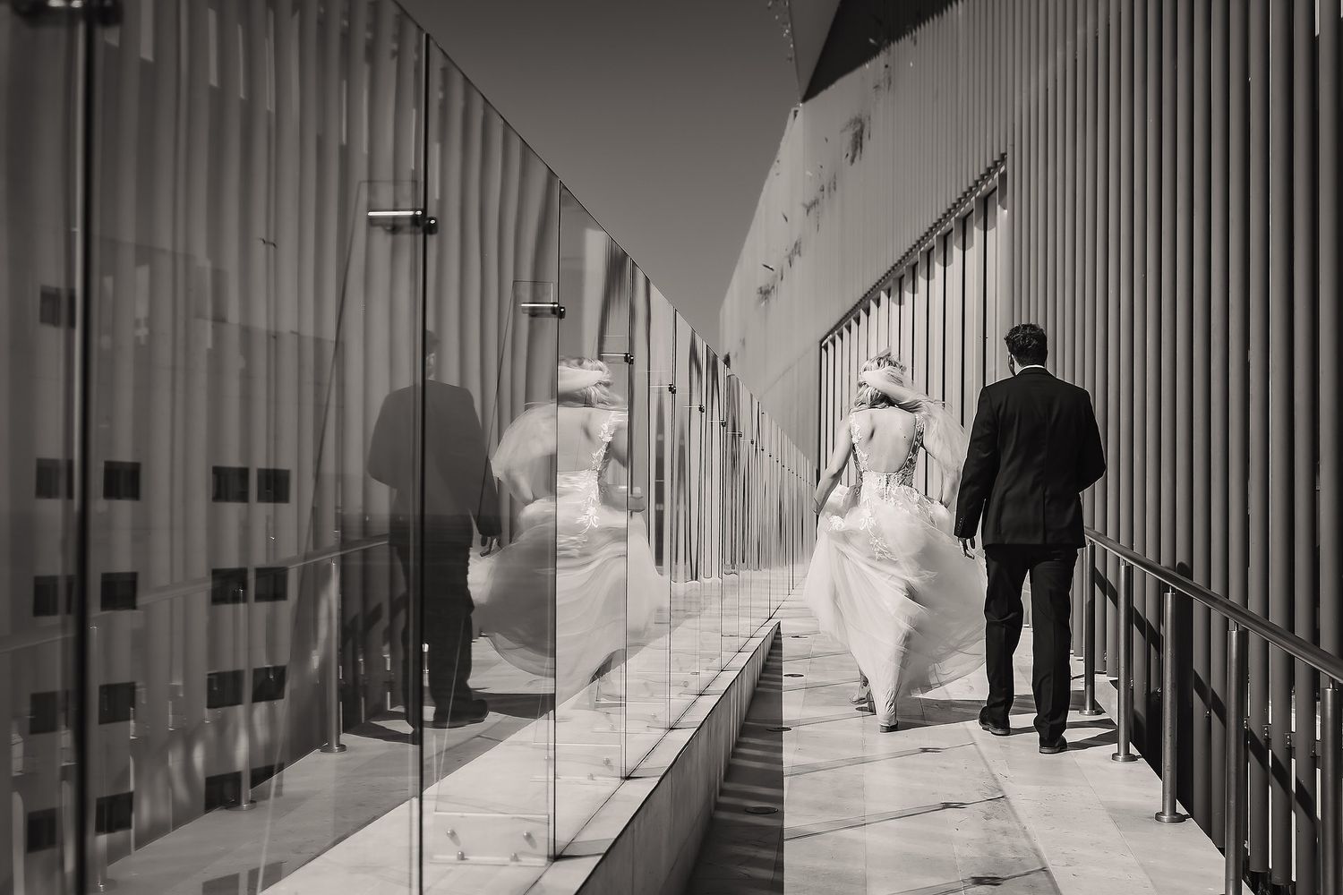 A modern architectural corridor with white walls and vertical metal bars creating dramatic shadows and lines.