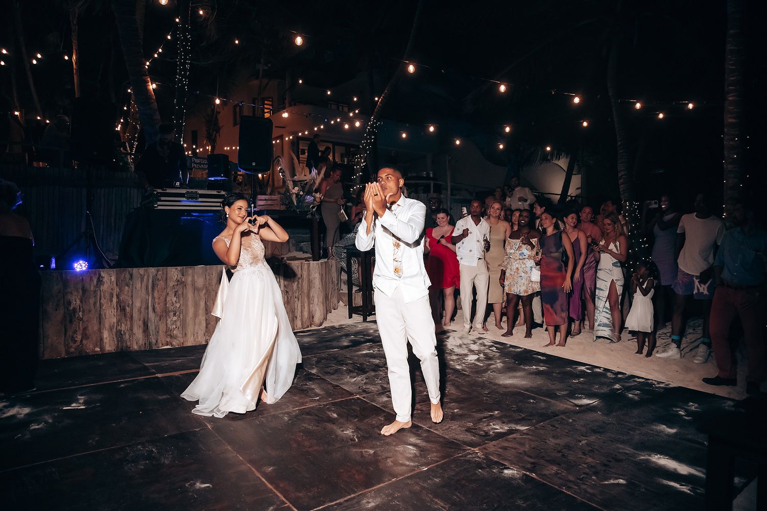 Wedding reception dance floor lit by string lights at night with guests celebrating.