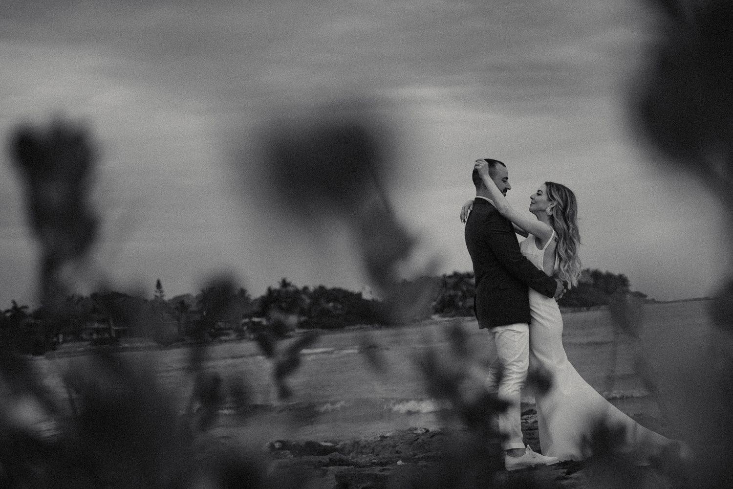 Romantic black and white photo of newlyweds embracing at sunset on the beach.