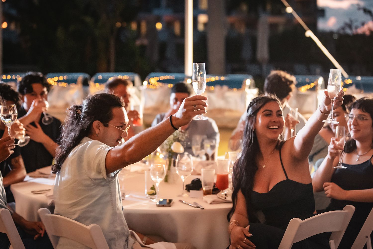 Guests raising champagne glasses in a toast at an elegant outdoor evening wedding reception celebration.