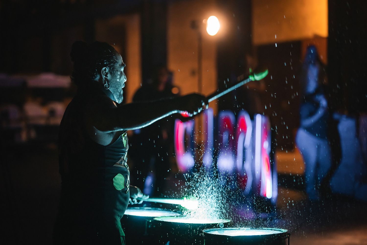 Performer splashing water with a glowing stick during a dramatic nighttime light show performance.