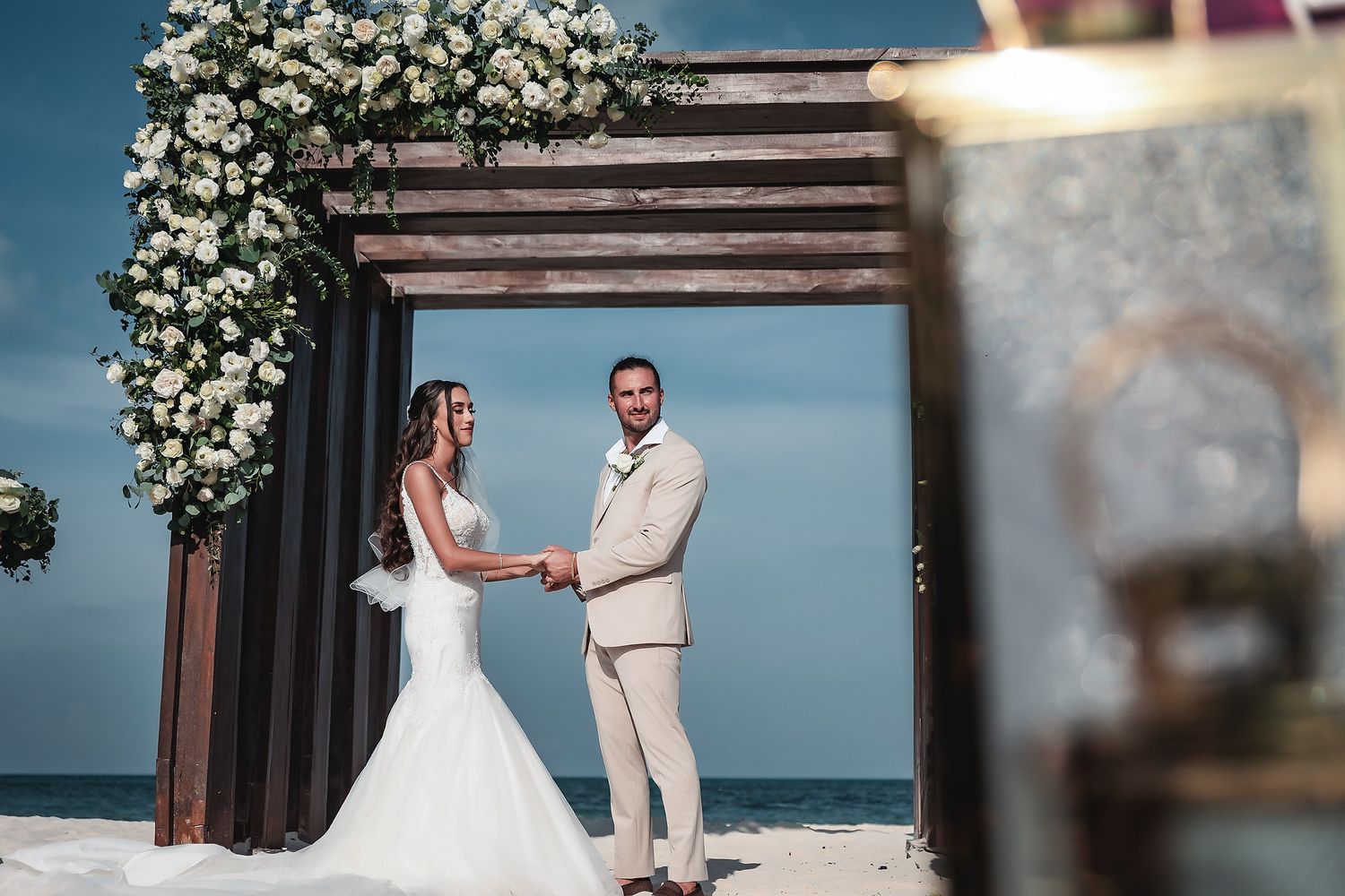 Bride and groom holding hands under a floral arch on a beach wedding ceremony with ocean views.