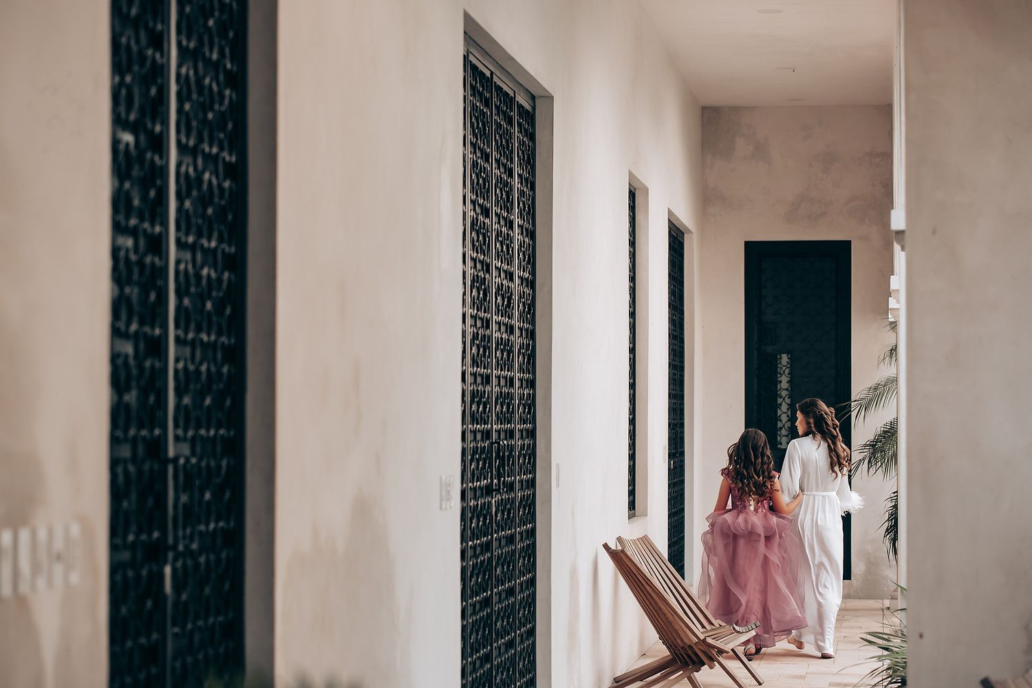 A person in a pink dress stands in a bright white hallway with dark patterned walls creating a dramatic contrast.