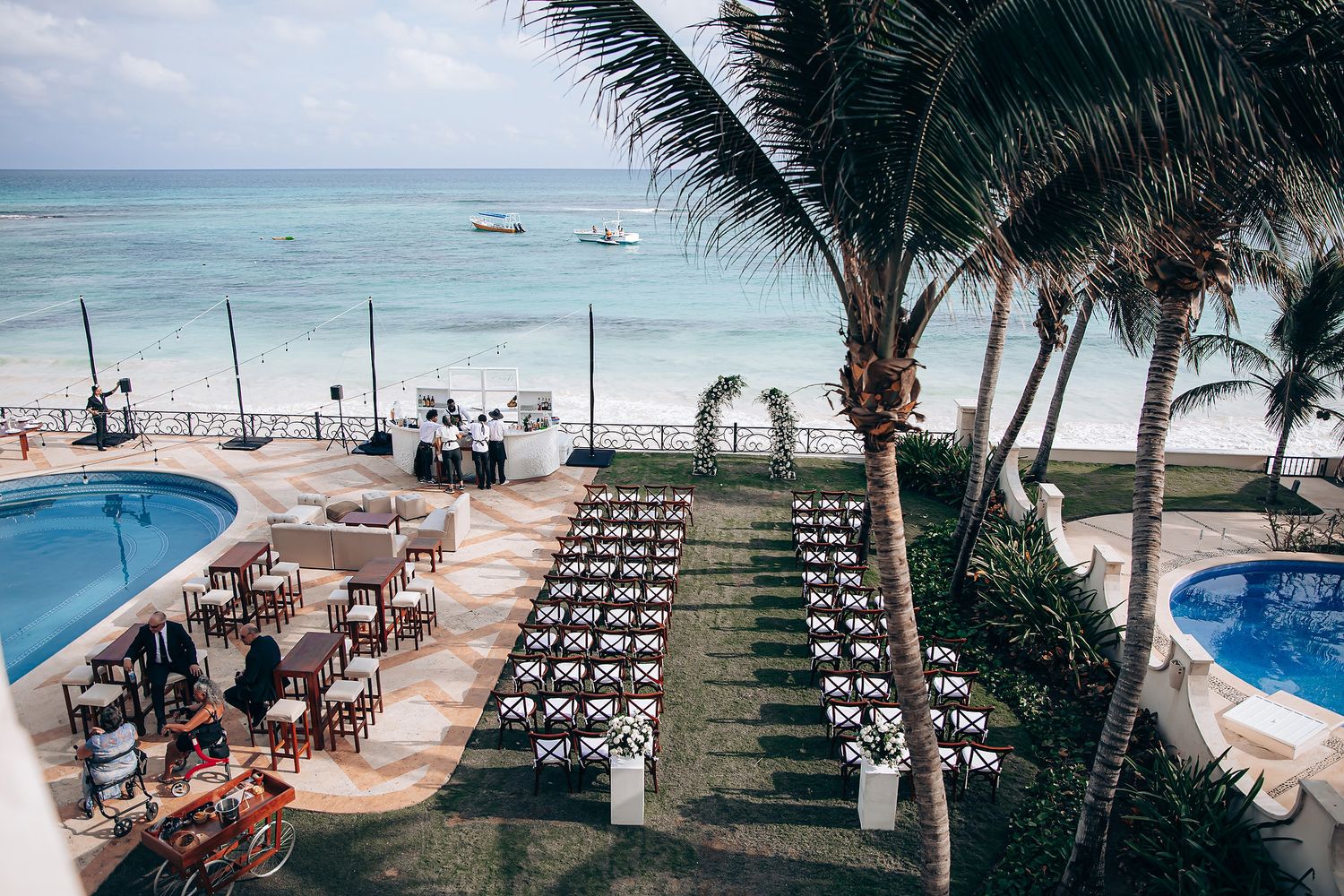 Scenic beachfront resort with palm trees, swimming pools, and lounge chairs along a turquoise ocean coastline.