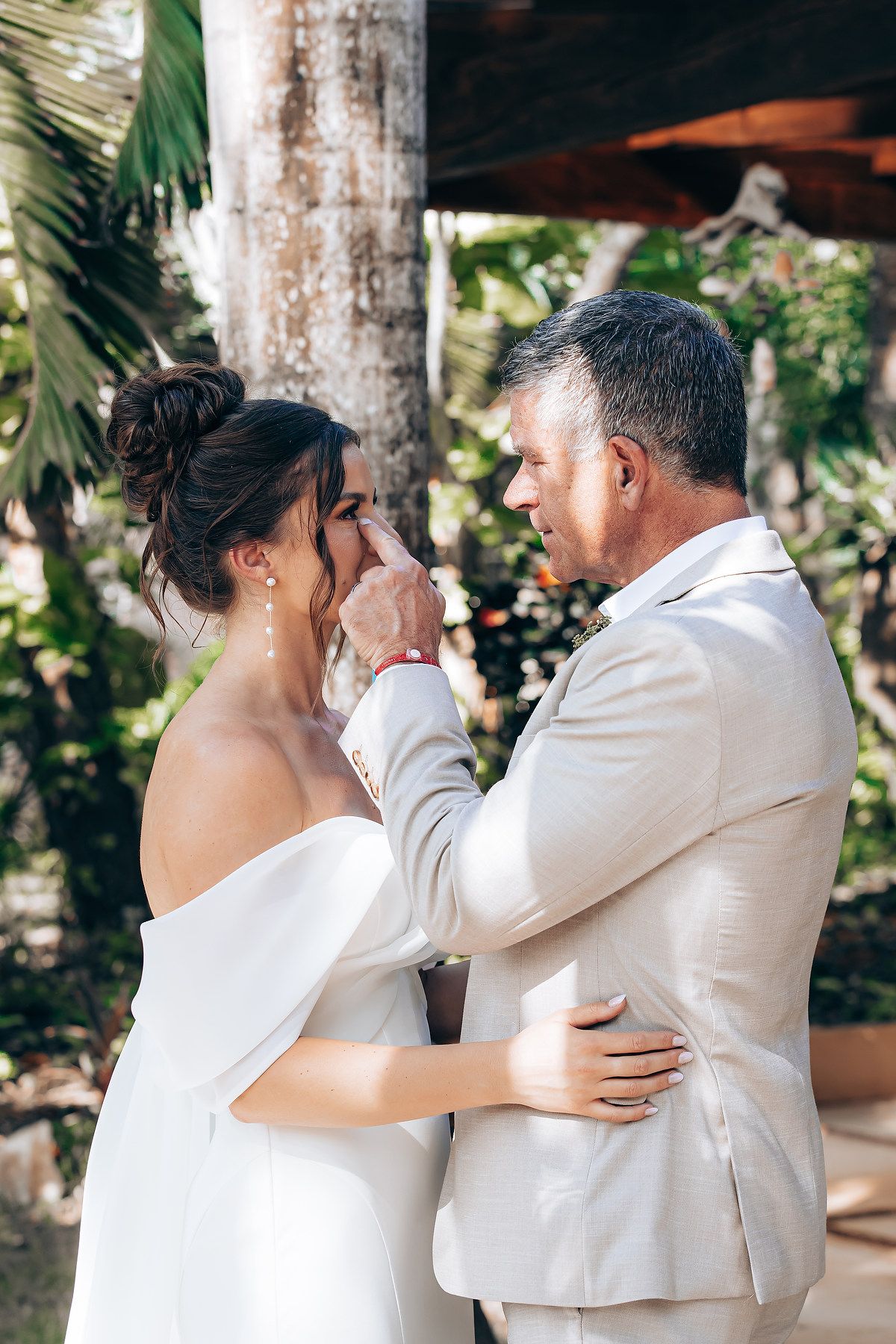 A couple shares an emotional moment during their outdoor wedding ceremony beneath palm trees and natural lighting.