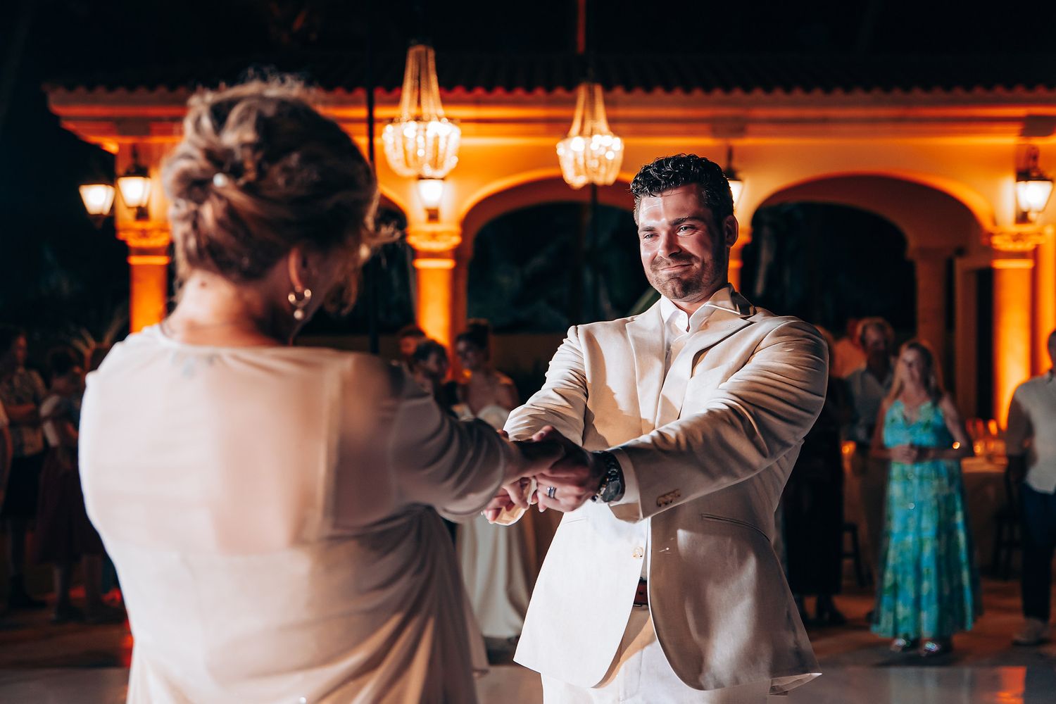 Newlyweds dance together under warm amber lighting at an evening wedding reception.