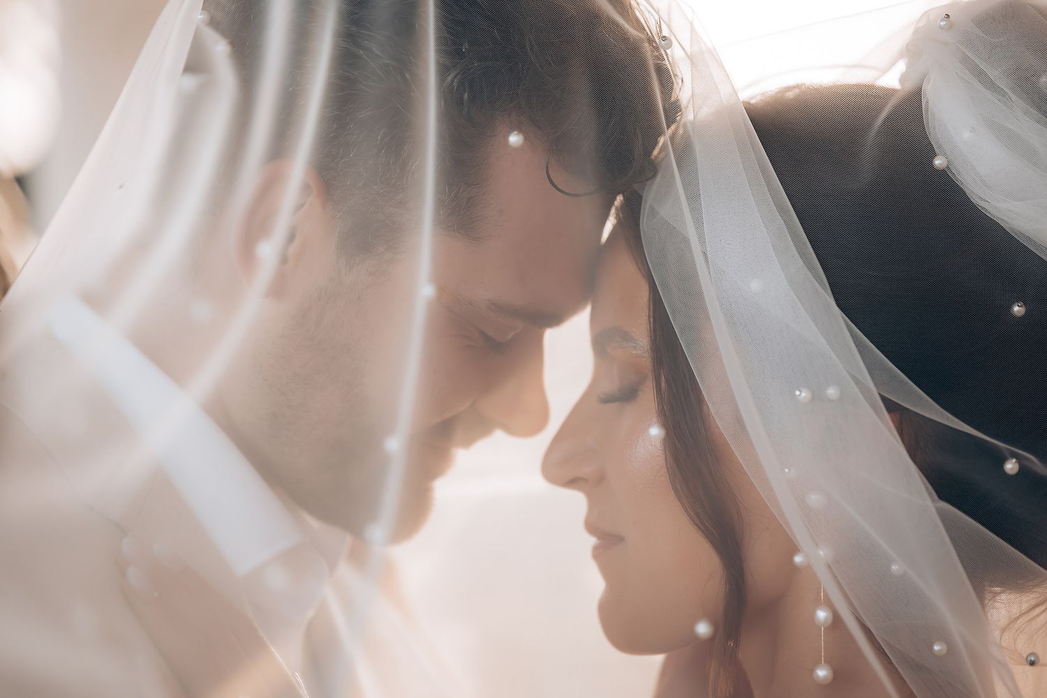 Romantic wedding couple embraces in soft sunlit hallway with wooden windows.