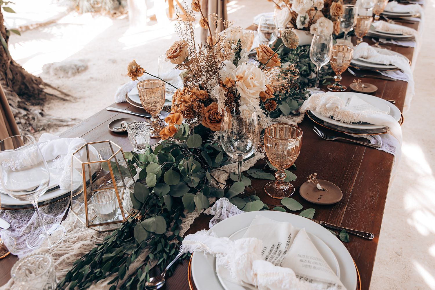 Elegant wedding table settings with white plates, crystal glasses, and floral centerpieces in a rustic venue.