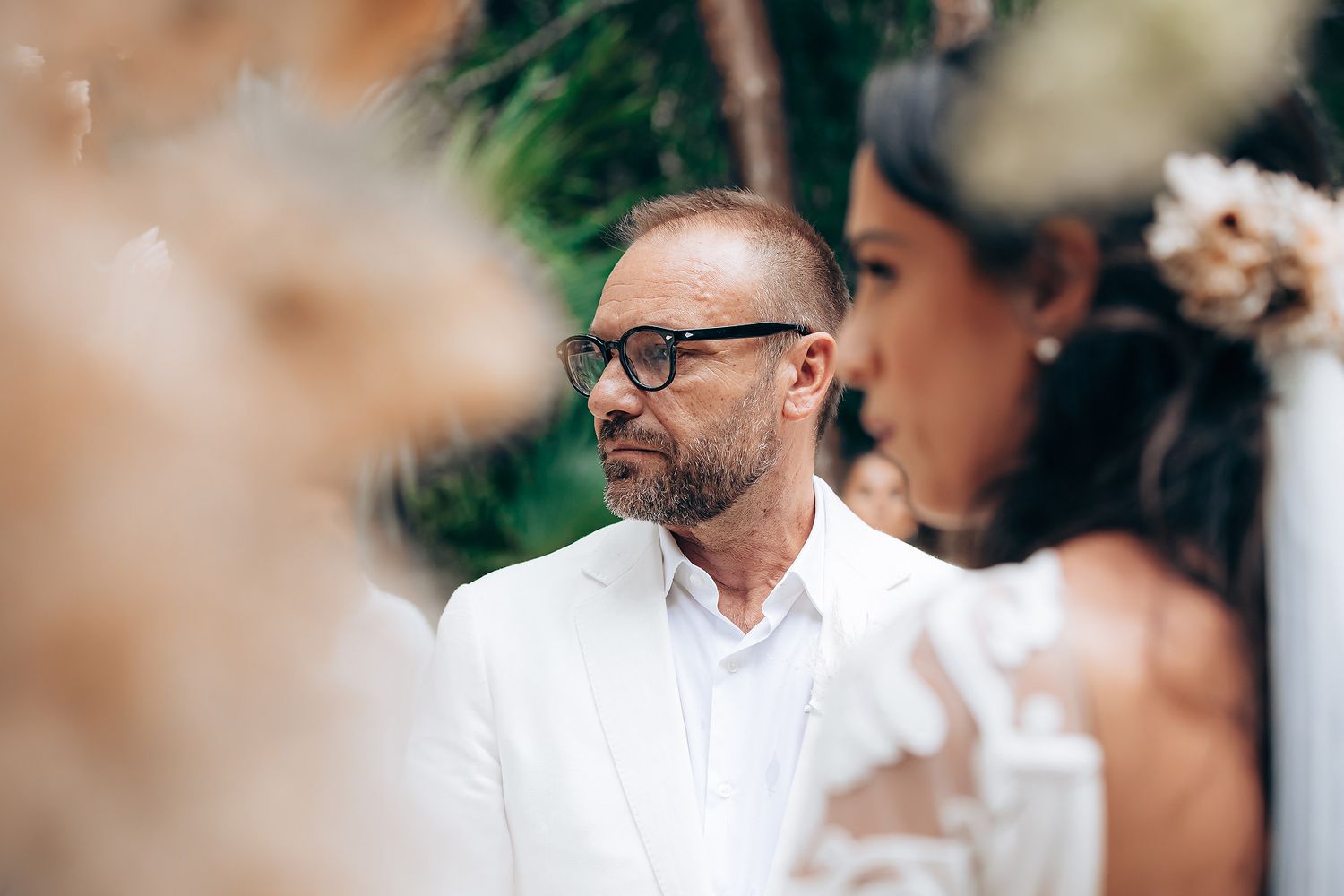 A person wearing glasses and a white dress shirt attends a wedding ceremony outdoors.