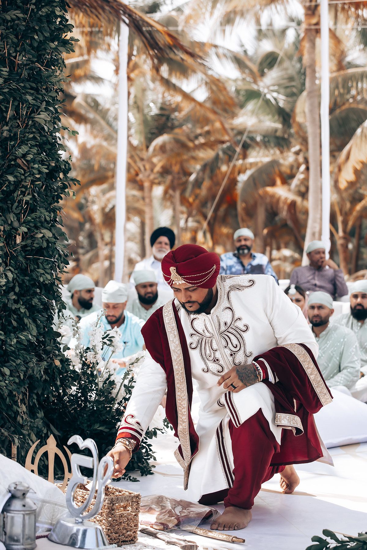 Traditional ceremony participants in burgundy and white attire seated on floor during cultural wedding ritual.