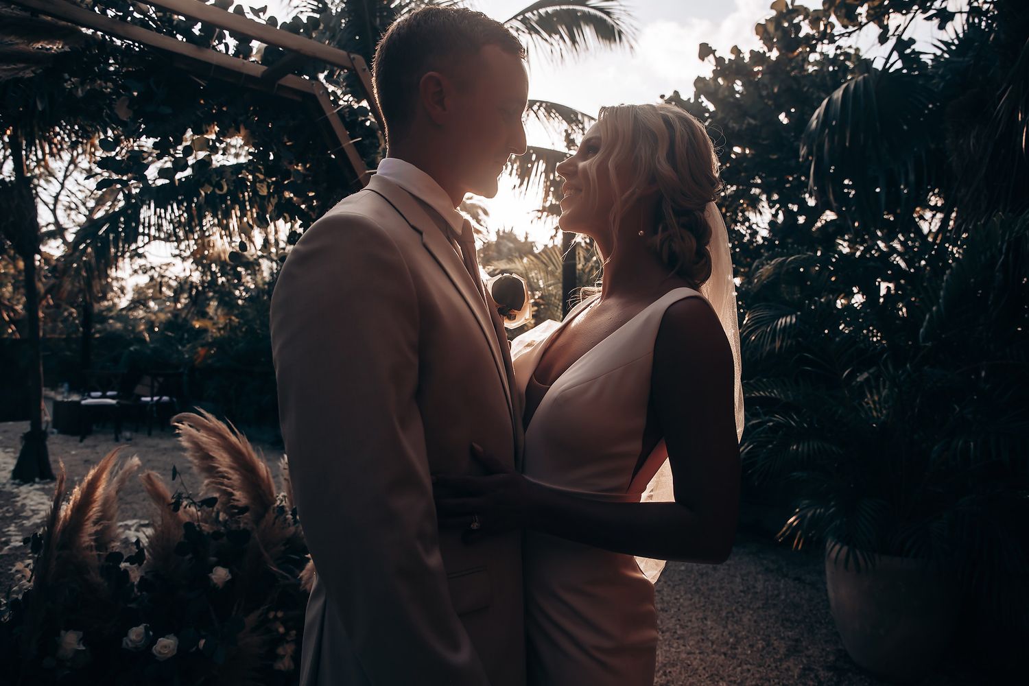 A romantic silhouette of a couple embracing at sunset with palm trees in the background.