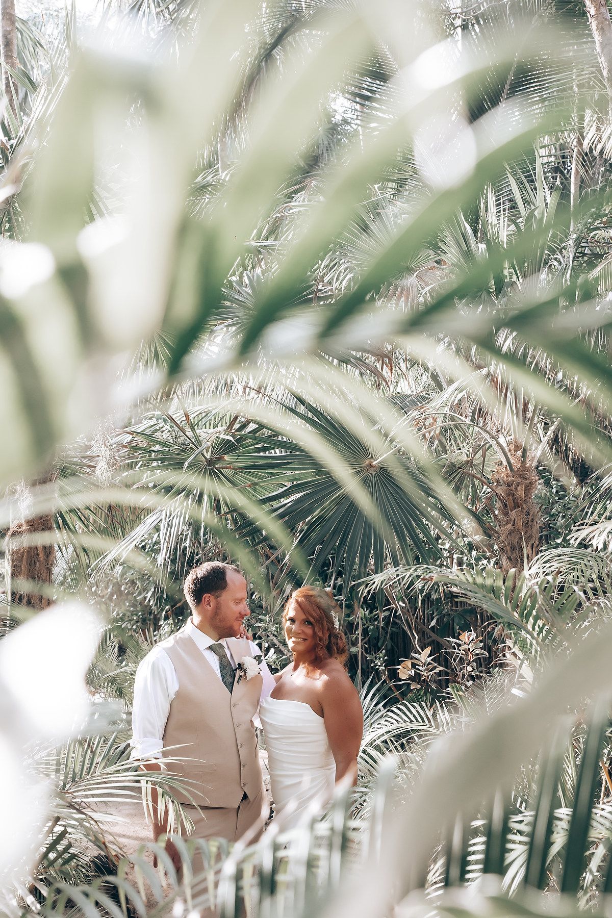 A couple shares a romantic moment among tropical palm trees in a beachside wedding setting.