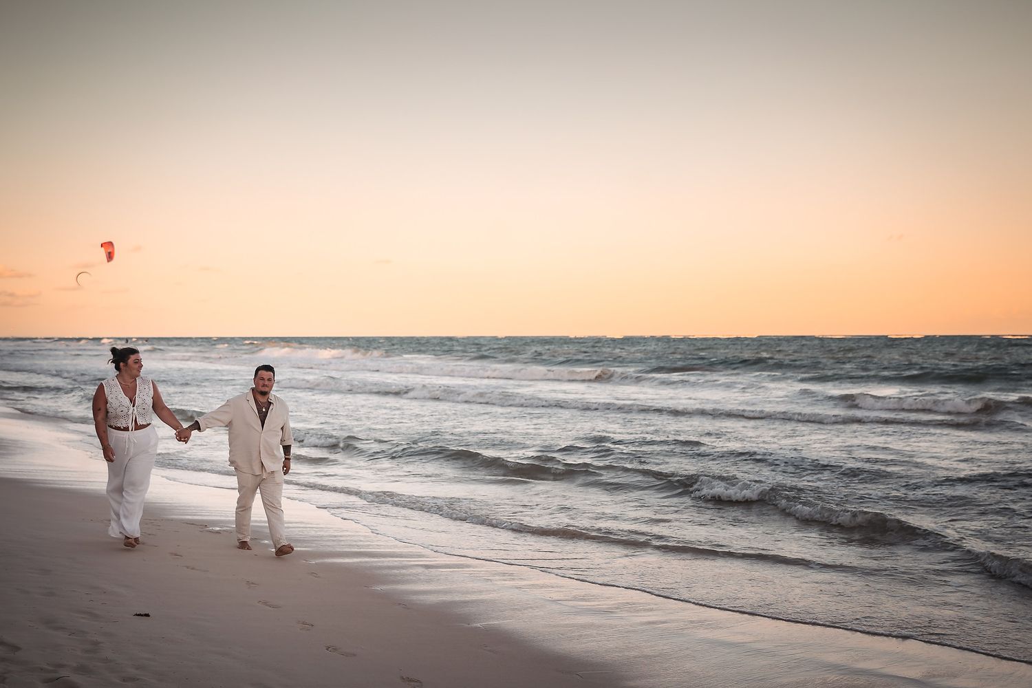 Couple holding hands while strolling on beach during golden hour.
