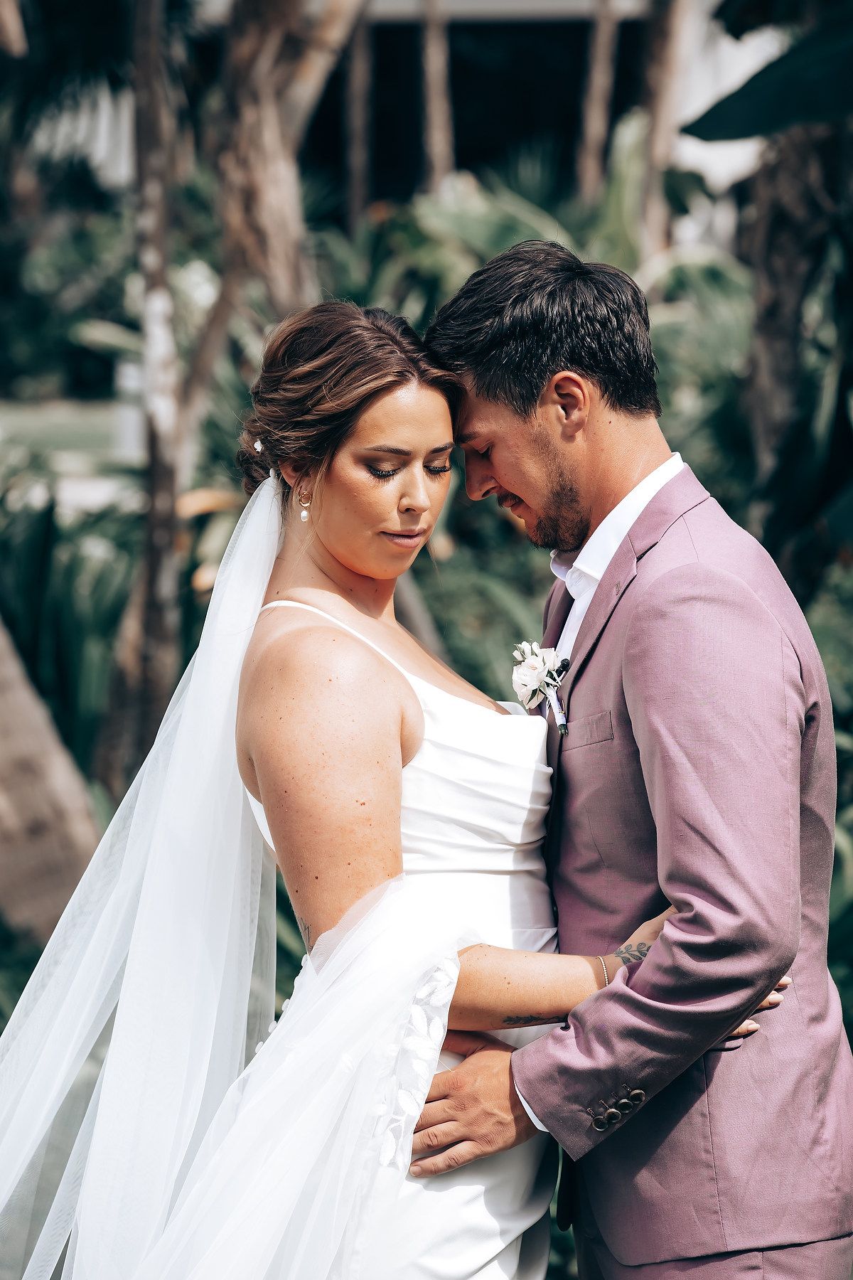 Romantic wedding couple embraces in an intimate outdoor moment wearing white and mauve attire.