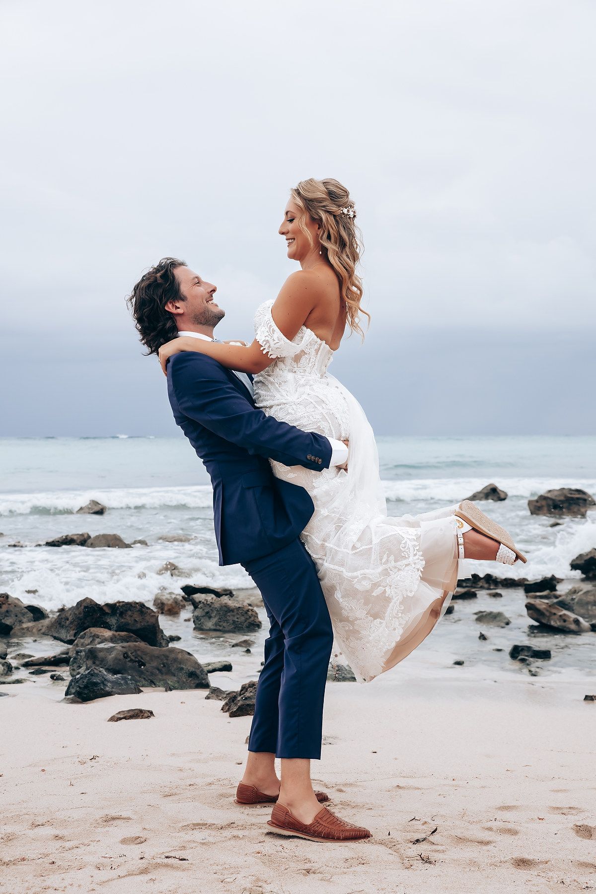 Playful couple embracing on a rocky beach during their wedding photoshoot.