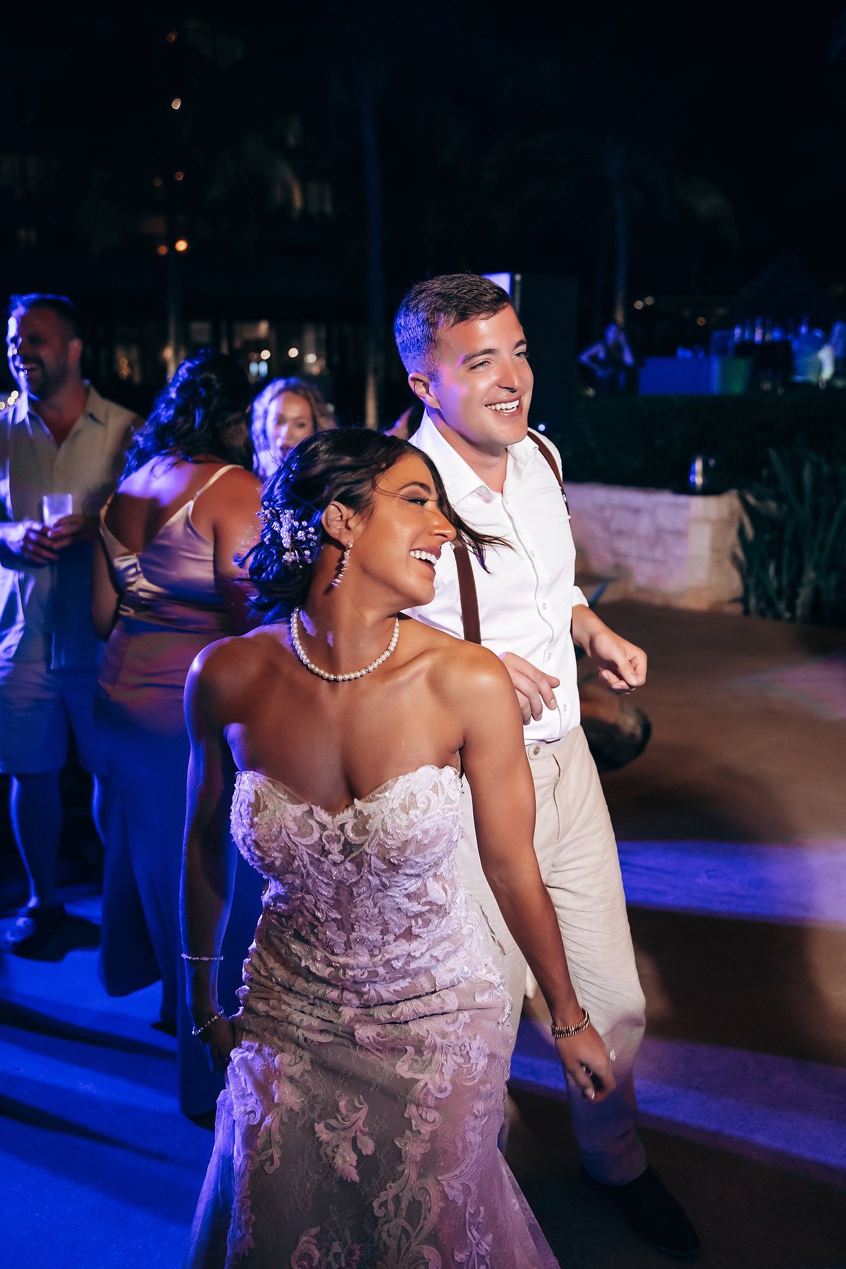 Wedding celebration on dance floor illuminated by blue lighting and string lights overhead.