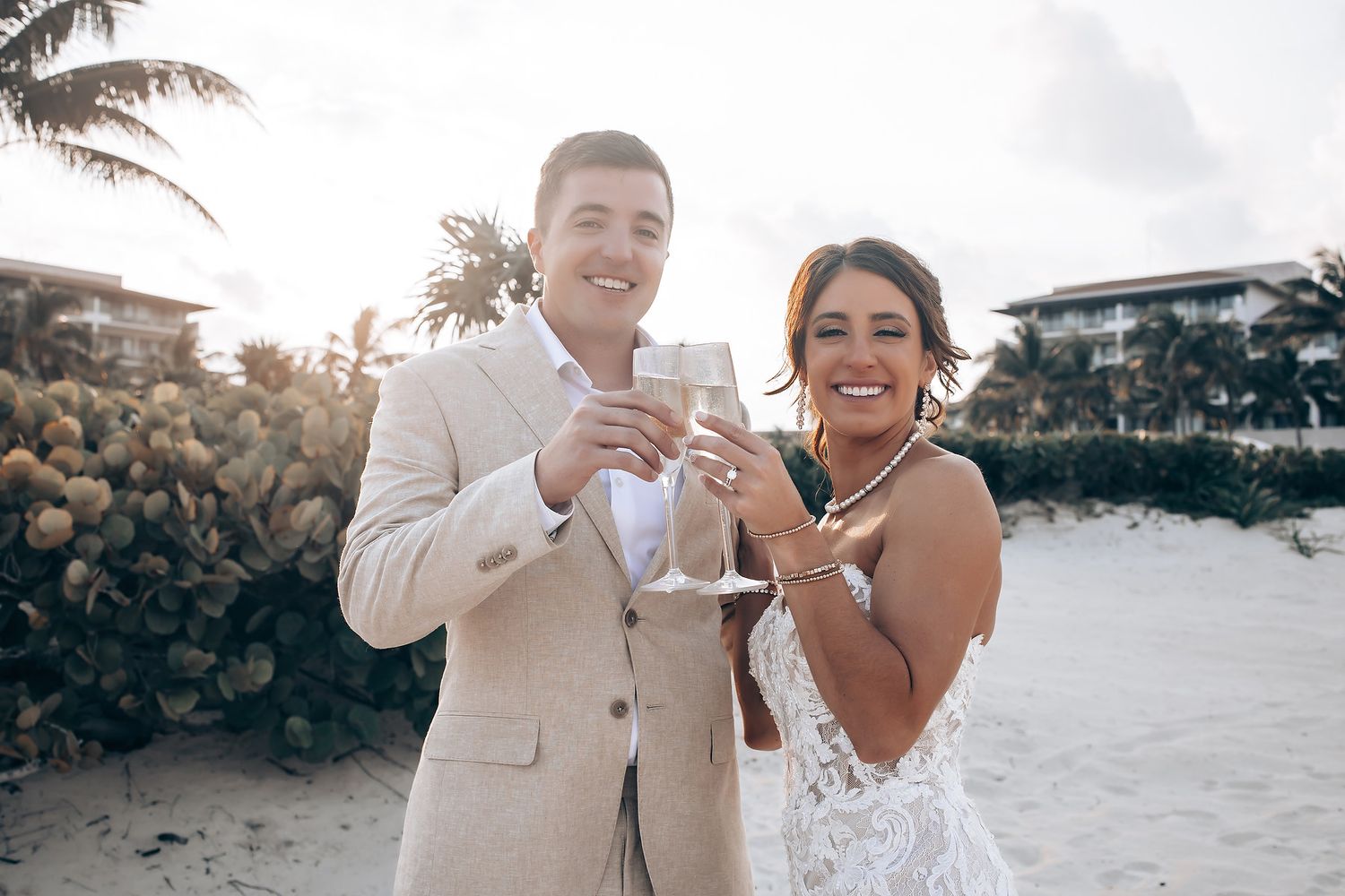 Joyful wedding celebration on a beach with palm trees at sunset.