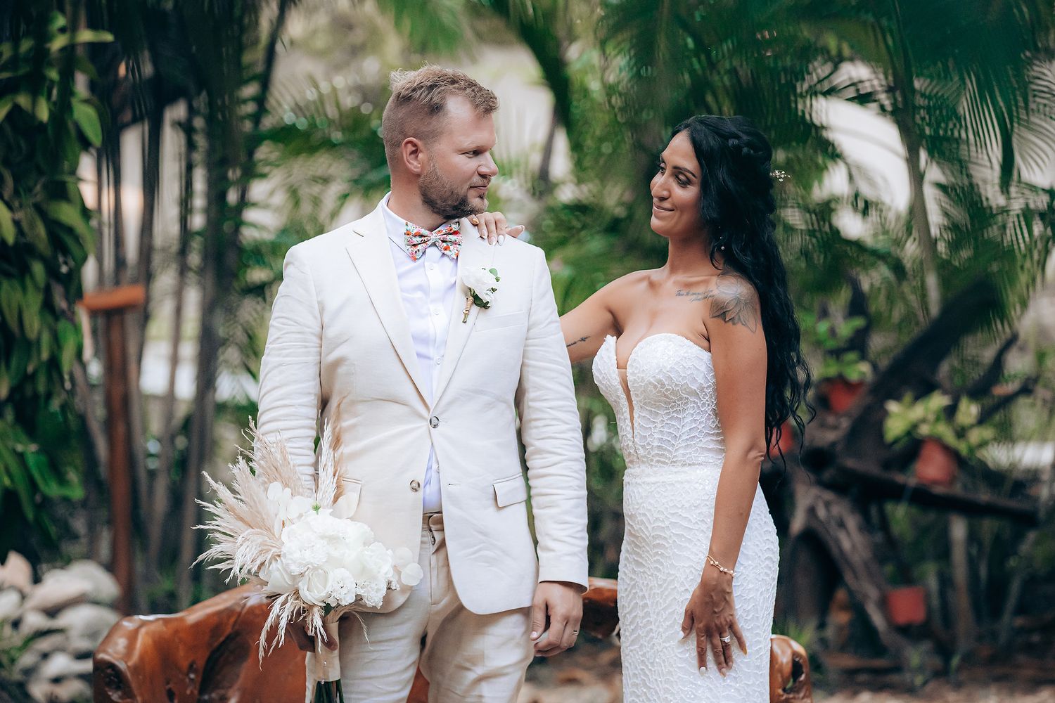 Elegant wedding couple in white attire posing in lush tropical garden.