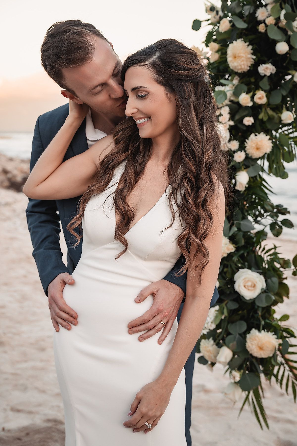 Intimate wedding couple moment captured near floral arch on beach.