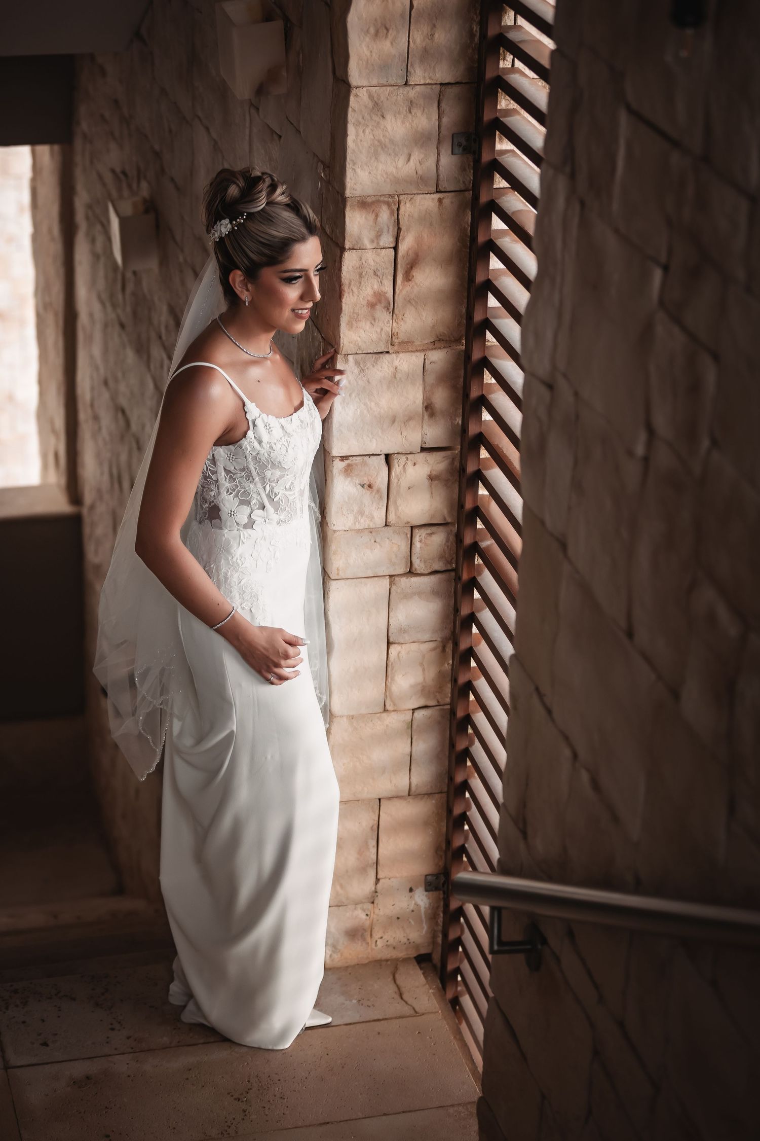 A bride in an elegant white gown poses near rustic brick walls and wooden details.