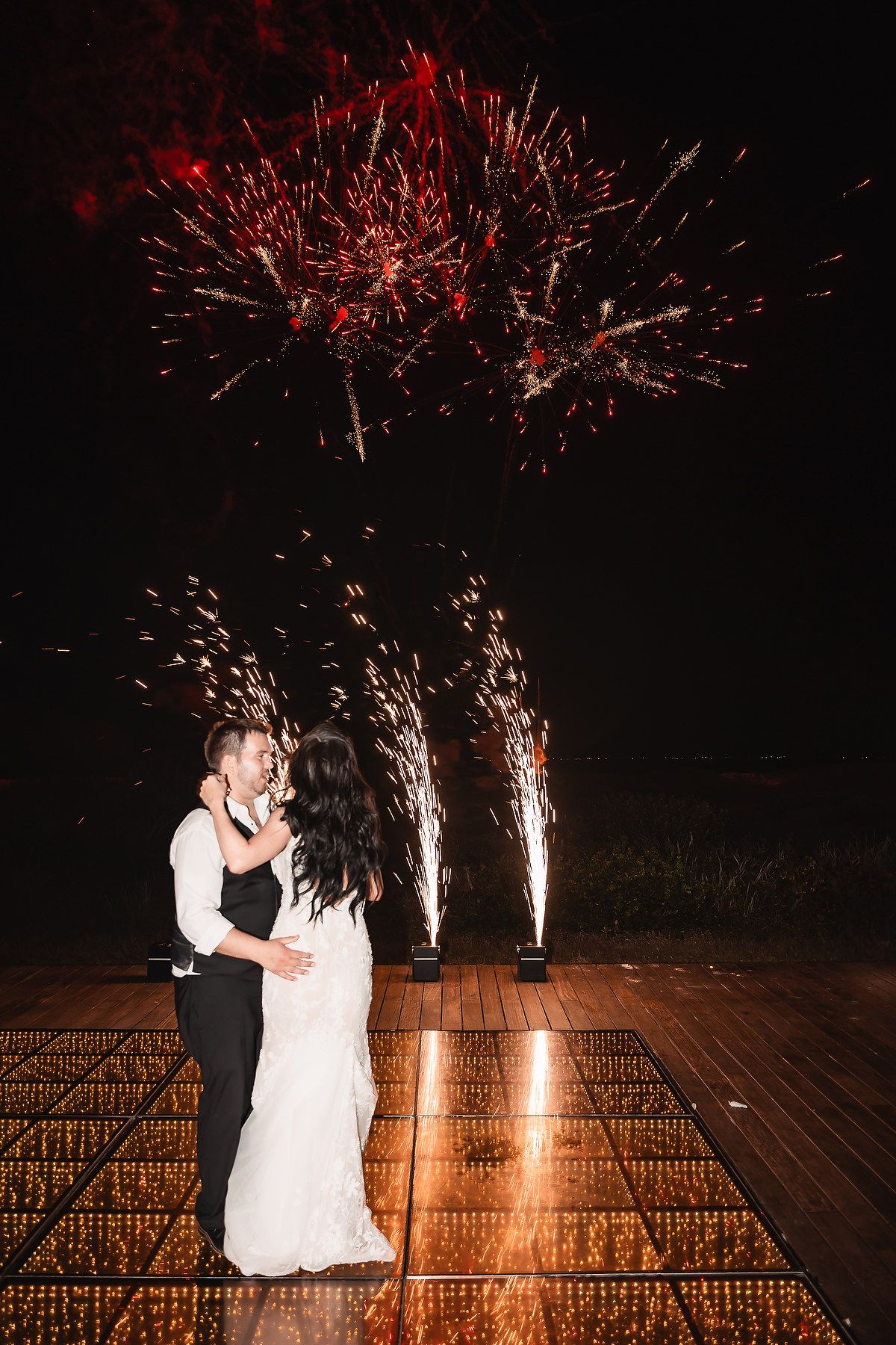 Couple shares romantic dance moment with sparkling fireworks display in background.
