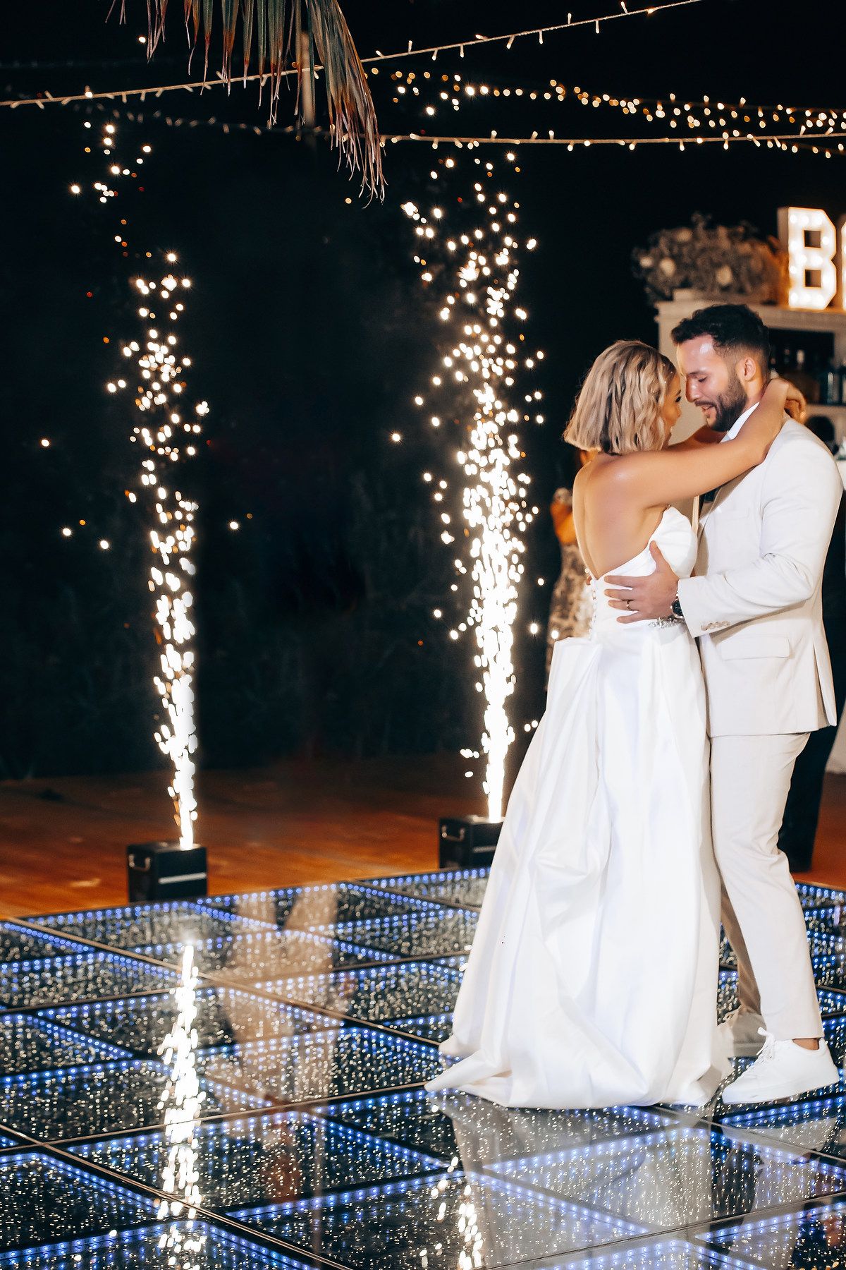 Couple dancing on an illuminated LED dance floor with sparkler fountains creating a magical atmosphere.