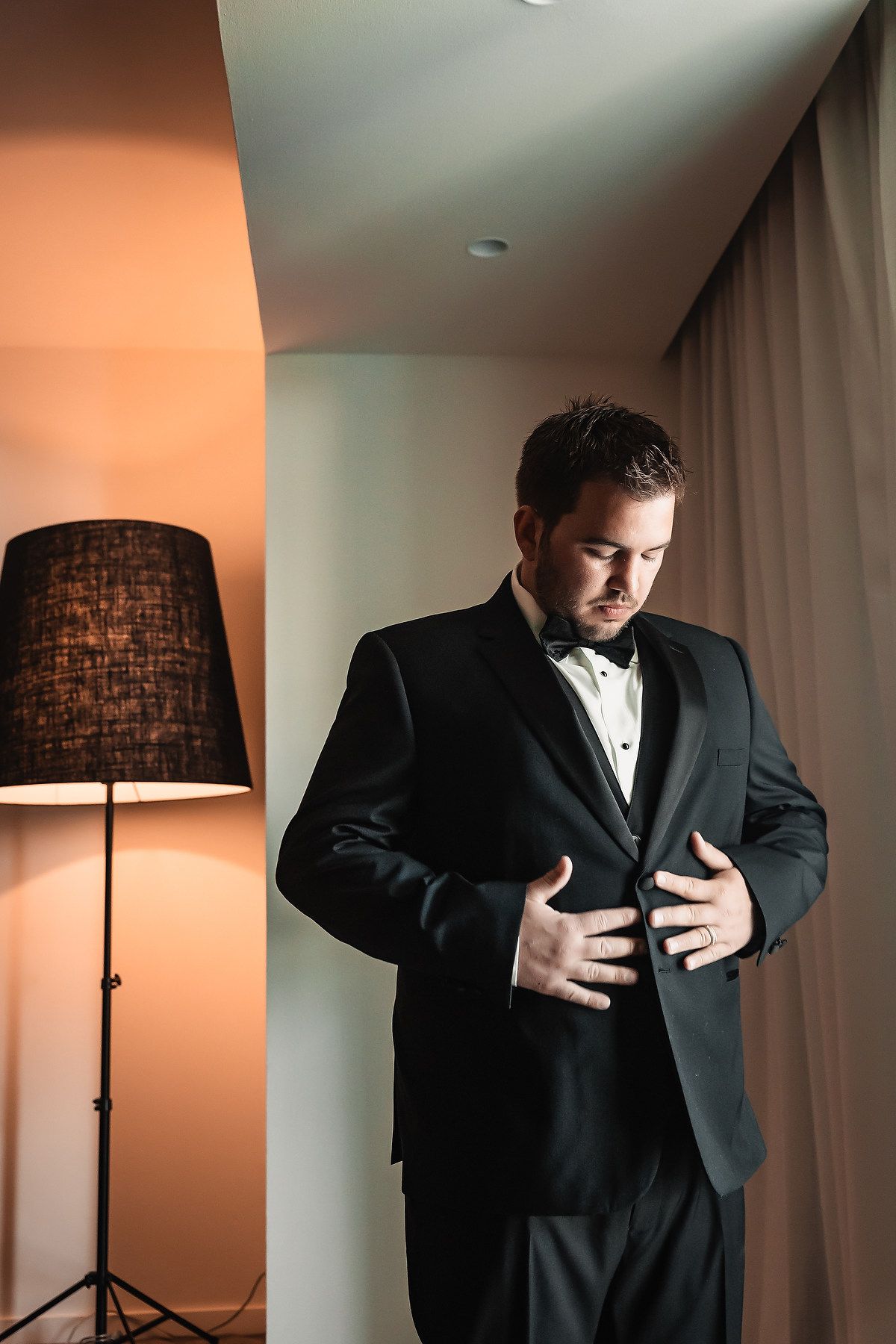 A series of artistic photos showing a groom adjusting his formal black tuxedo jacket in warm lighting with a floor lamp.