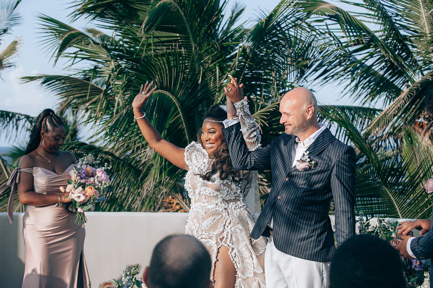 Wedding guests dance and celebrate together under swaying palm trees at an outdoor tropical reception.