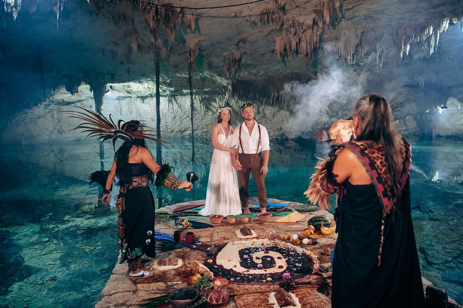 Underground cave wedding celebration with photographers capturing moments by pristine blue waters.