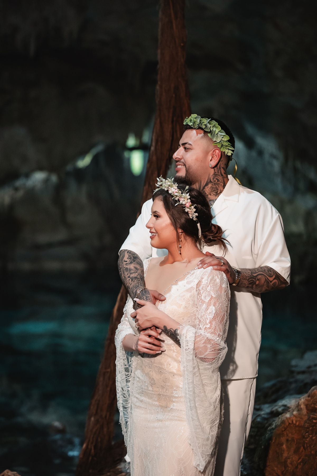Romantic couple sharing intimate moment in cave setting with floral crowns and white attire.
