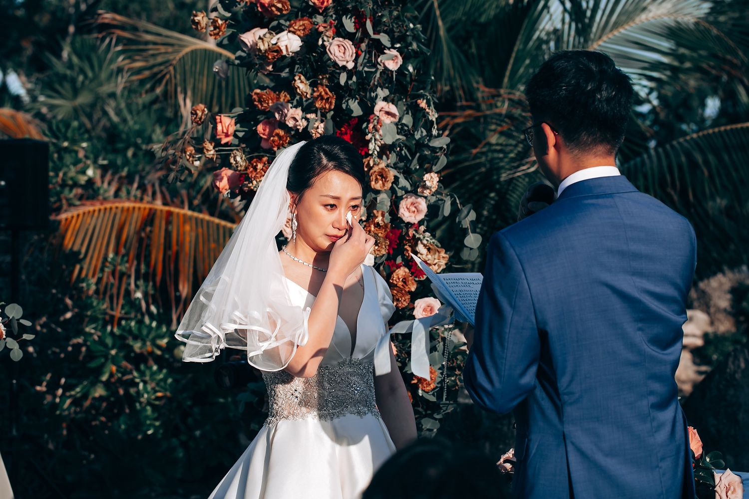 Intimate outdoor wedding ceremony with floral arch and tropical garden backdrop.