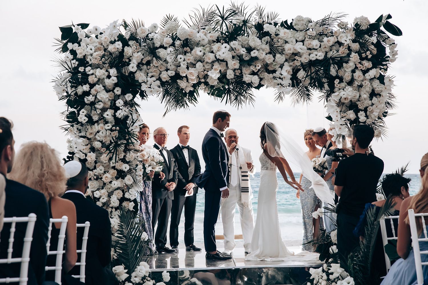 Wedding ceremony under a luxurious white floral arch overlooking the ocean.