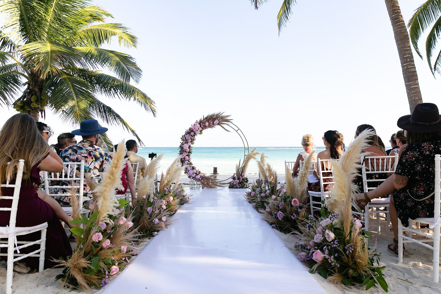 Panoramic view of a tropical beach bar with palm trees and guests enjoying drinks along the shoreline.