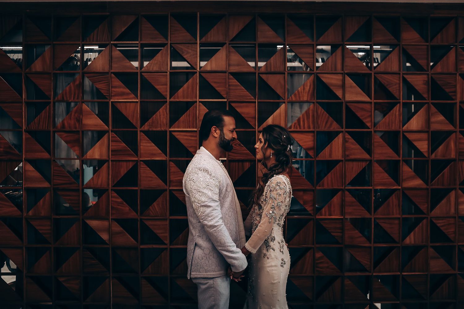 Wedding couple dances in front of a geometric red brick wall with dramatic lighting and shadows.