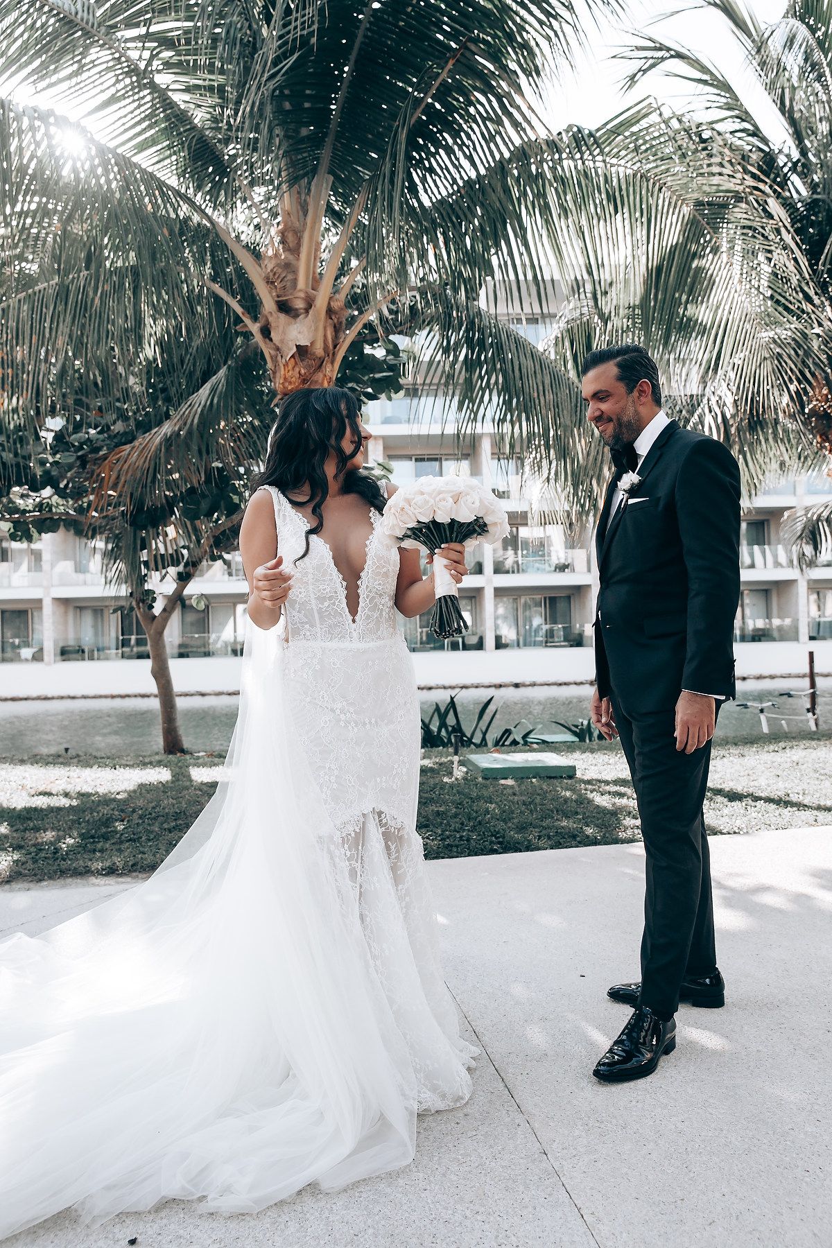 Romantic wedding photoshoot with palm trees and a flowing white gown on a tropical beach walkway.