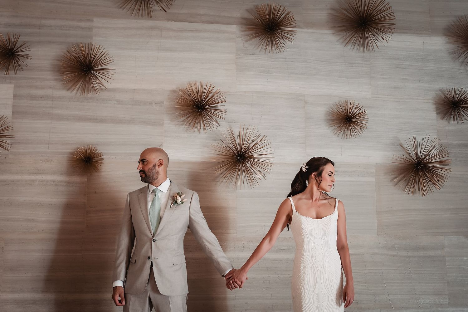 A couple holds hands against a wall decorated with starburst designs in a modern, minimalist wedding setting.