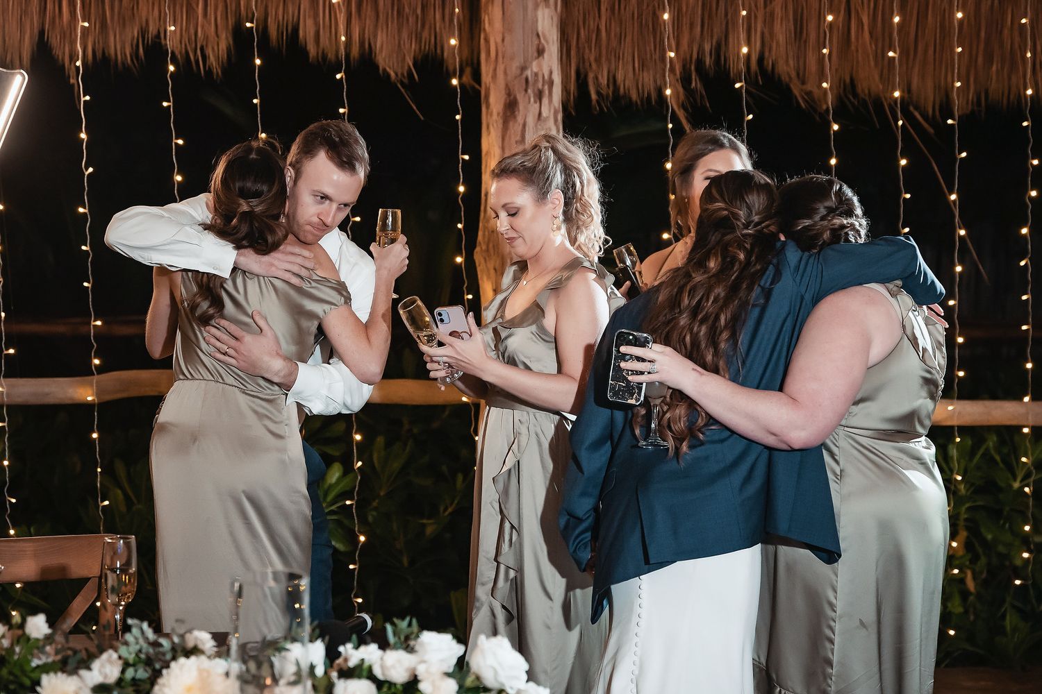 Wedding guests embracing and celebrating at a romantic reception venue with warm fairy lights in the background.