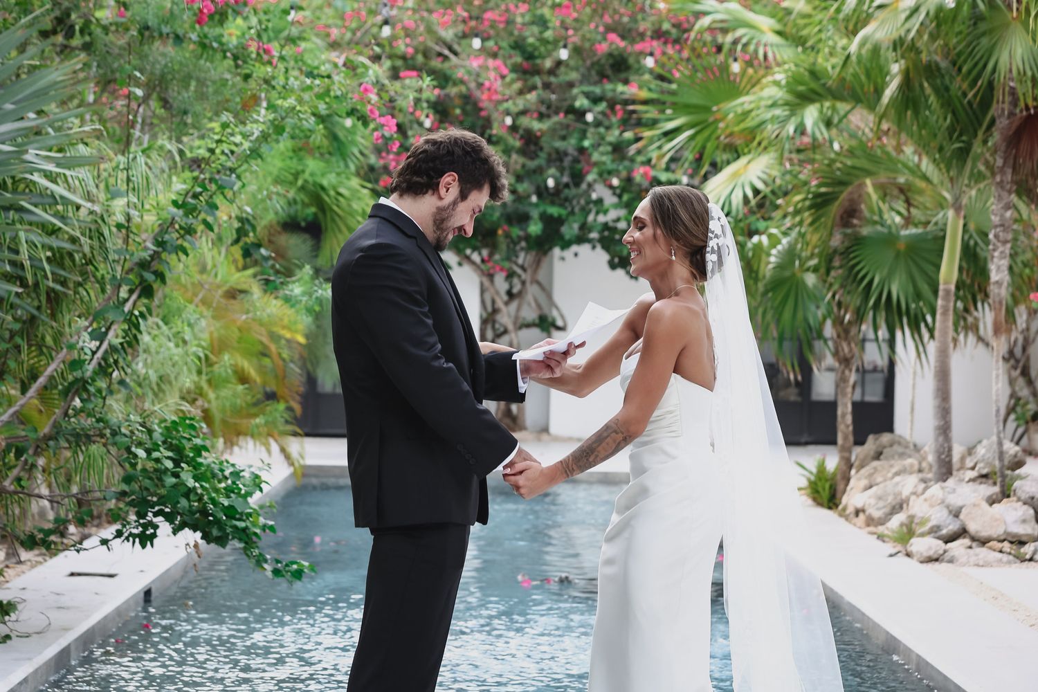 Bride and groom exchange vows by a tropical pool, surrounded by lush greenery on their wedding day.