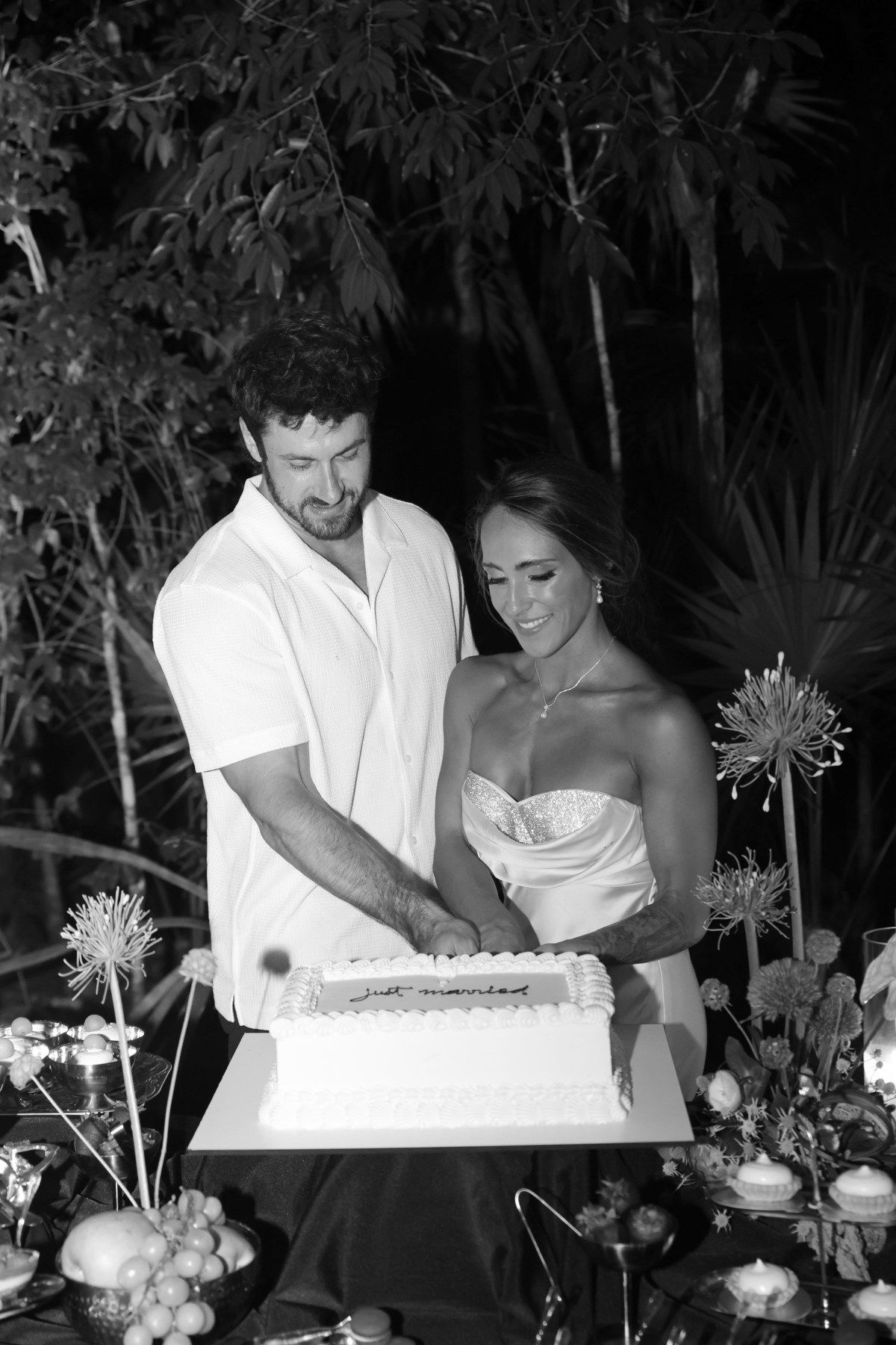 Newlyweds cut their wedding cake outdoors at night in a black and white photo.