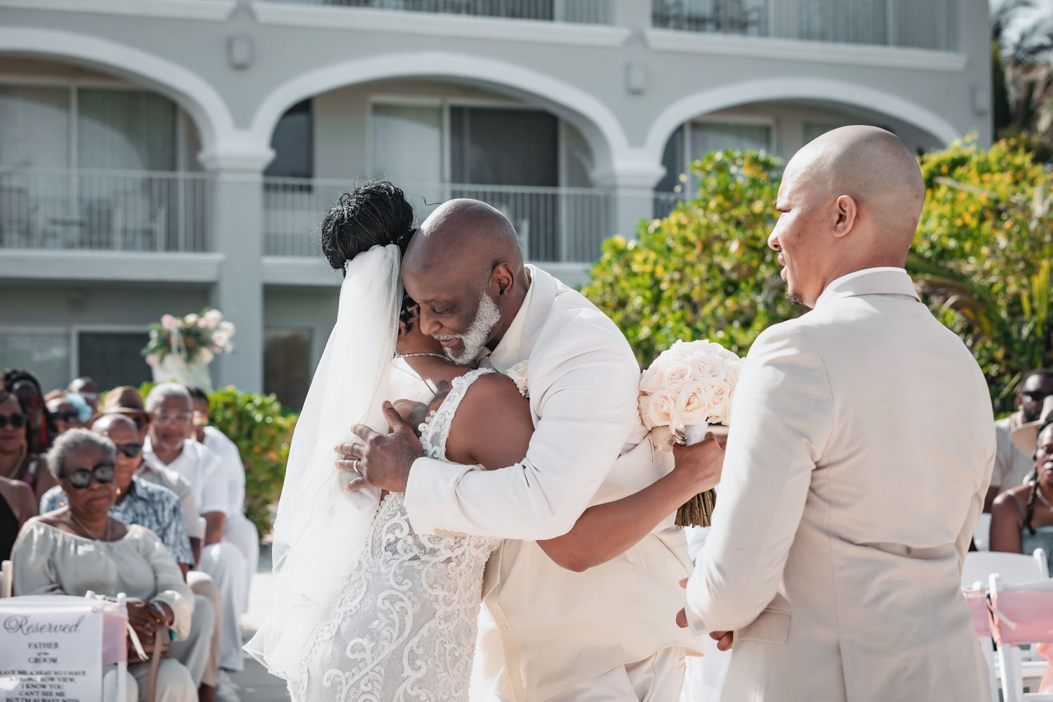 Emotional wedding moment as bride receives warm hug from officiant during outdoor ceremony.