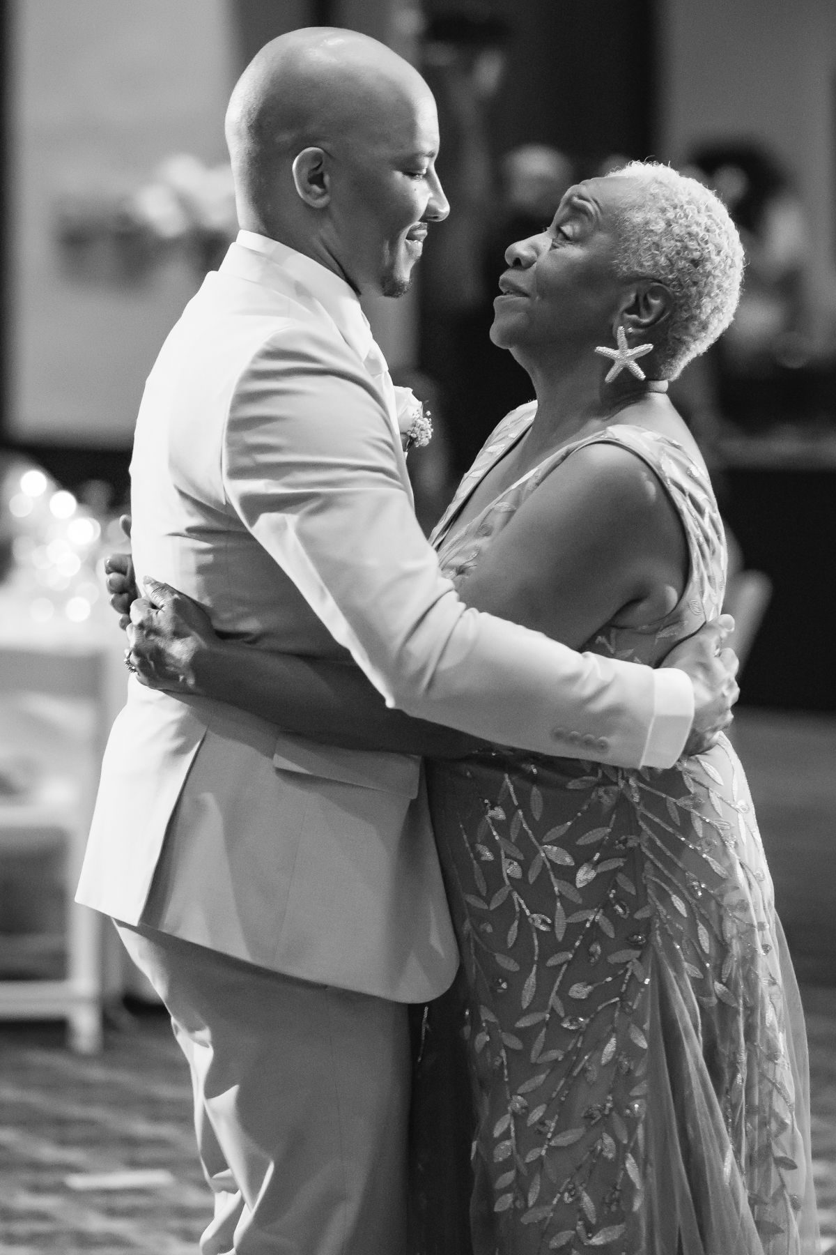 Black and white photo of a groom and his mother sharing an emotional dance at a wedding reception.