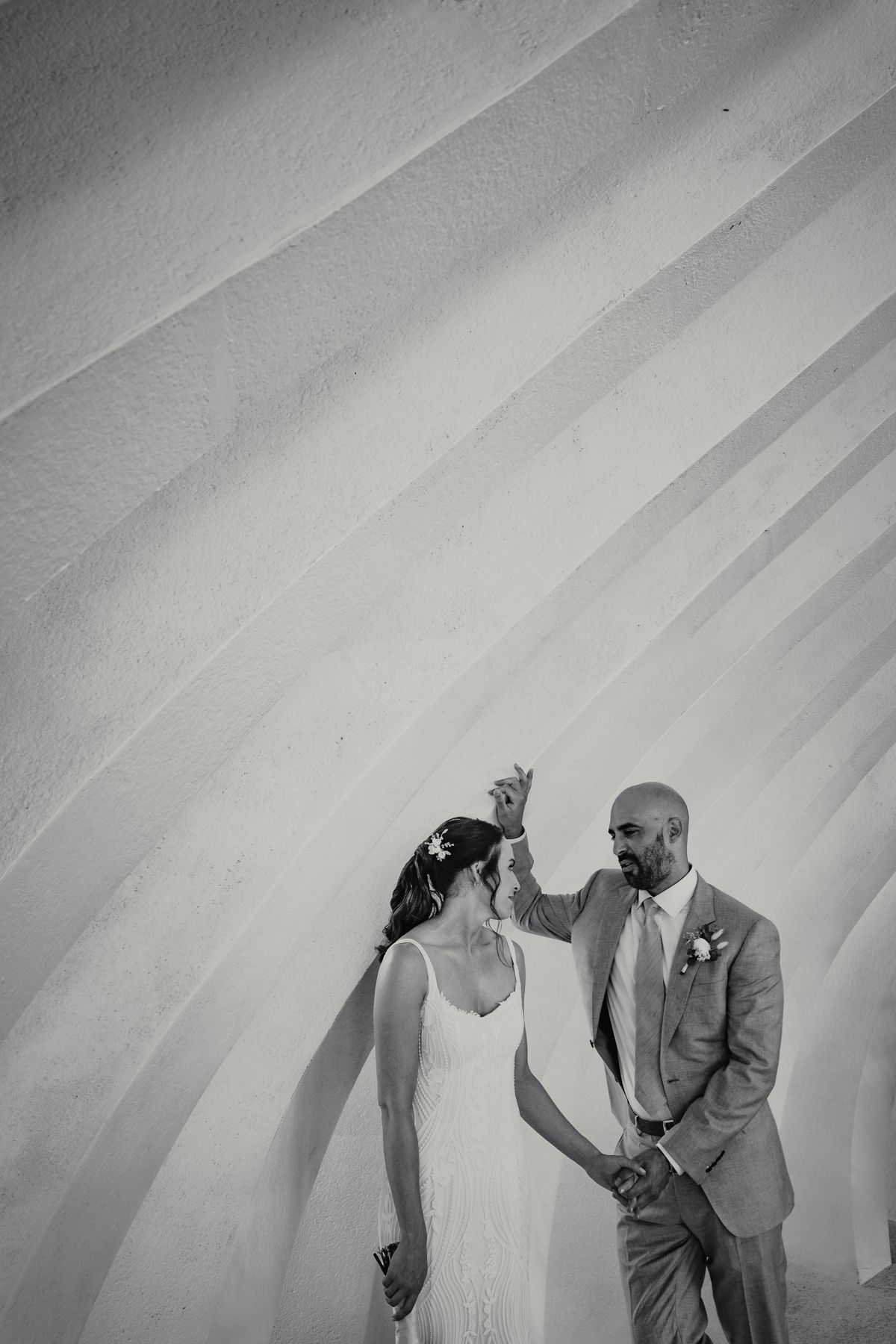 Black and white photo of a bride and groom holding hands against a geometric striped wall.