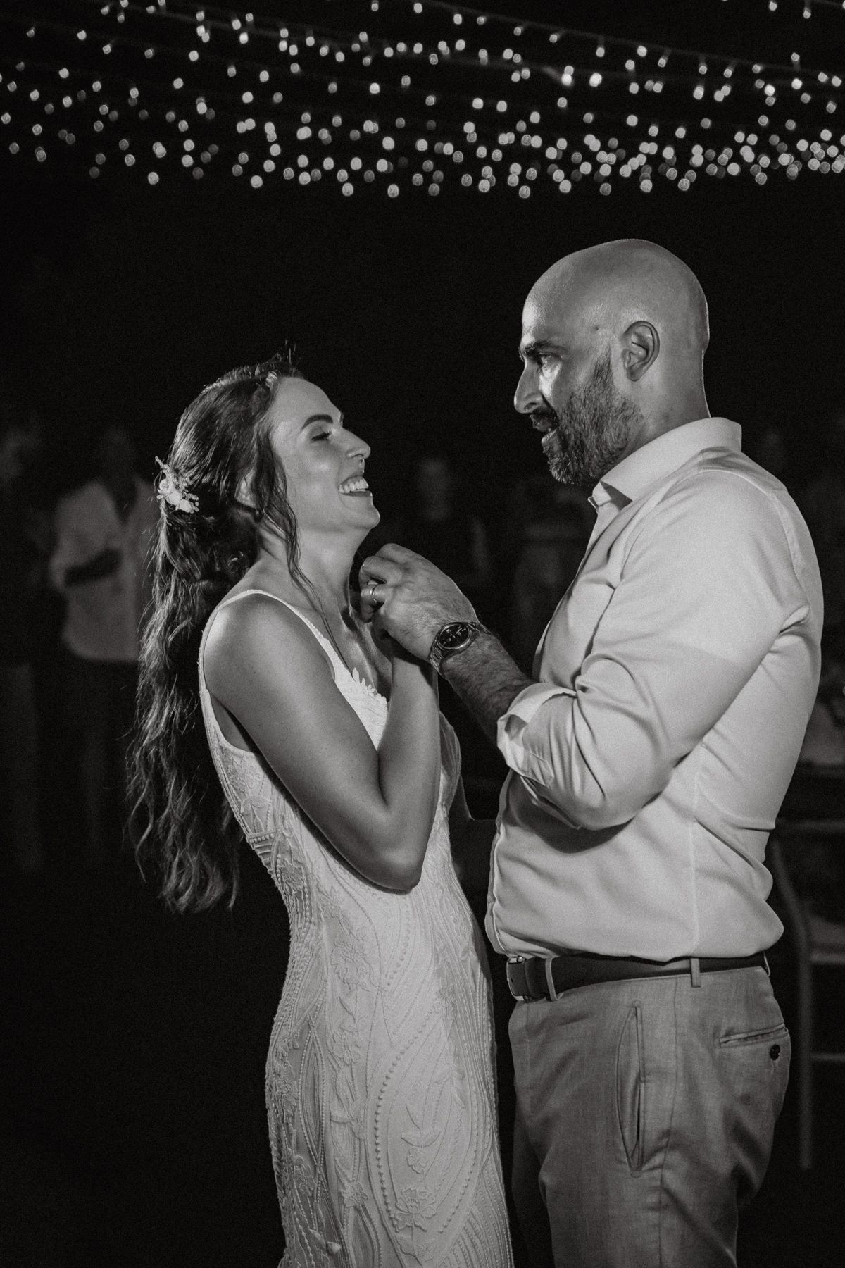 Black and white photo of a smiling bride and groom sharing their first dance at a wedding reception.