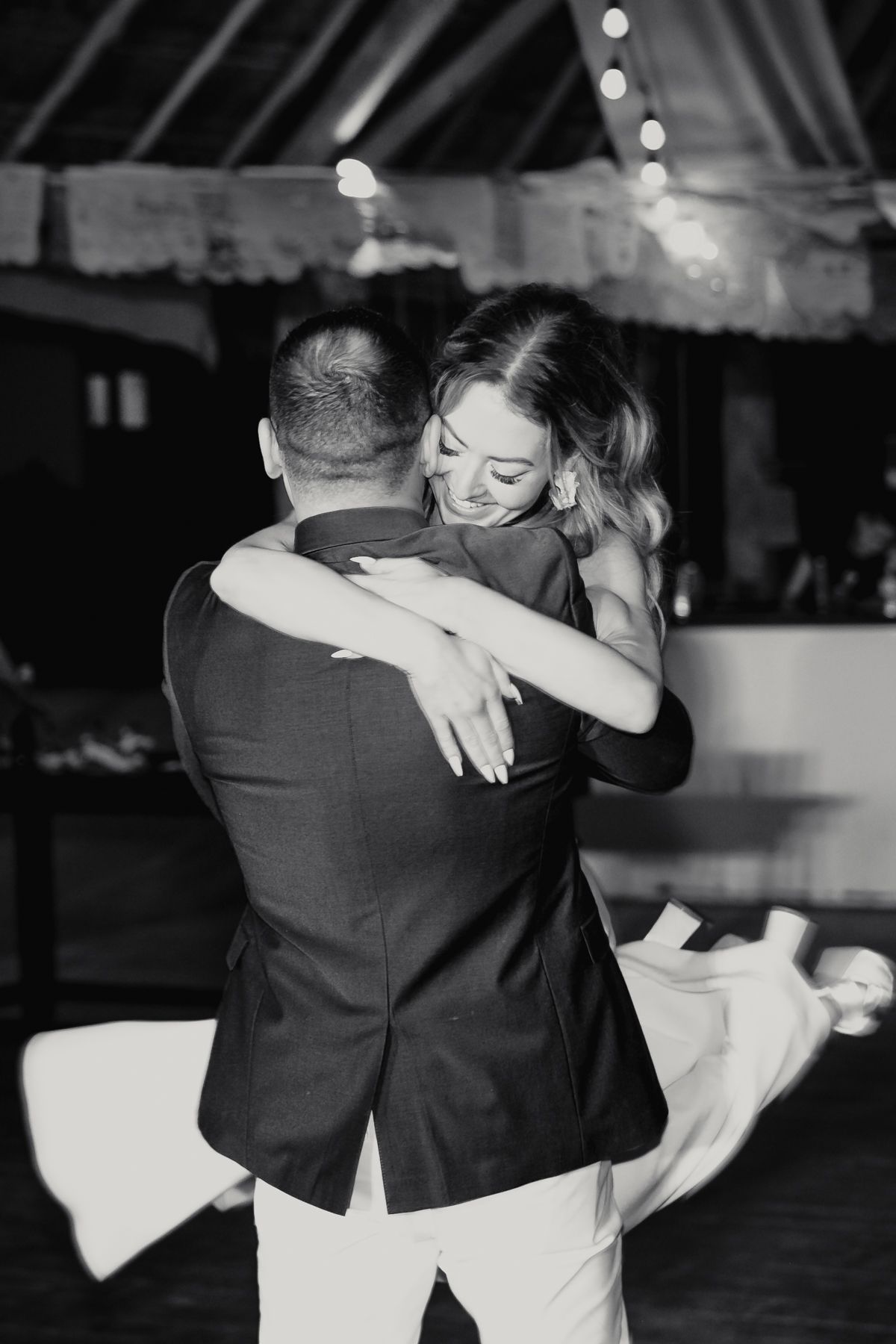 Black and white photo of a couple sharing a romantic first dance embrace at a wedding reception.