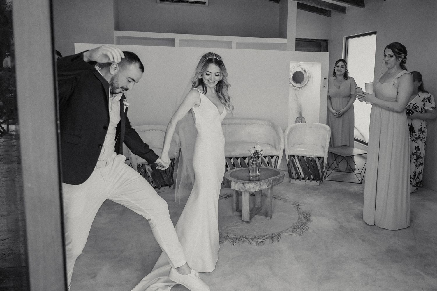 Black and white photo of bride and groom participating in traditional wedding ritual with guests watching indoors.