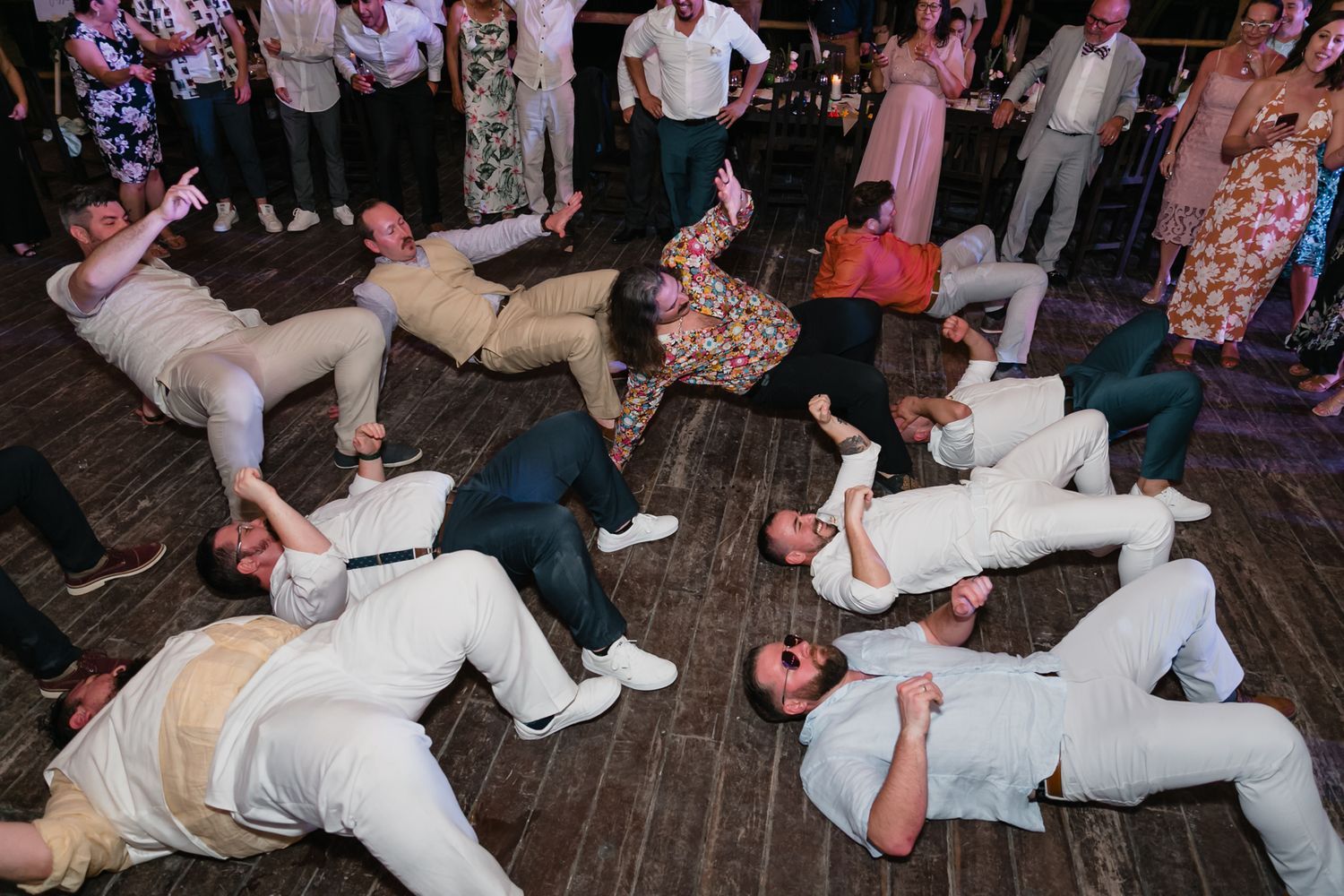 Wedding guests perform synchronized floor dance routine at lively tropical beach wedding reception celebration.