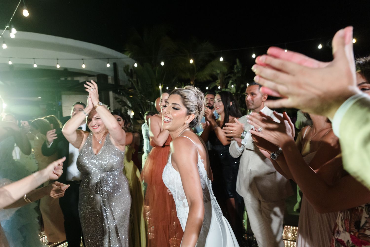 Bride in white gown dancing joyfully with guests at outdoor evening wedding reception celebration.