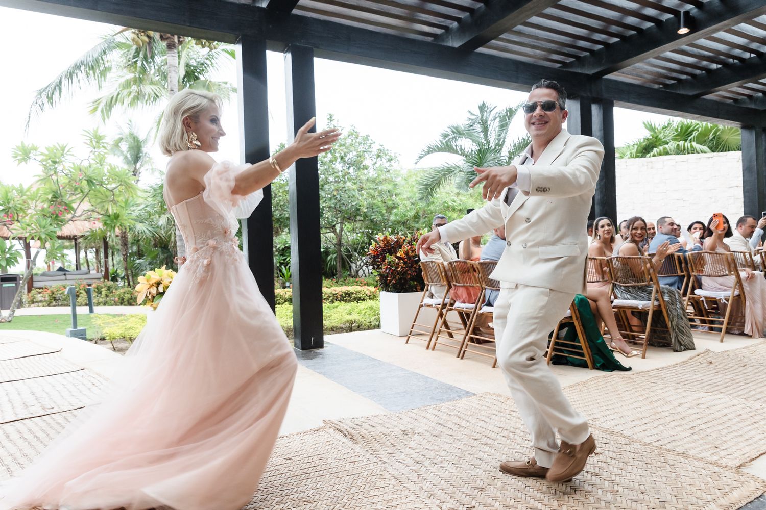 Bride in blush gown and groom in white suit share first dance at outdoor wedding reception.